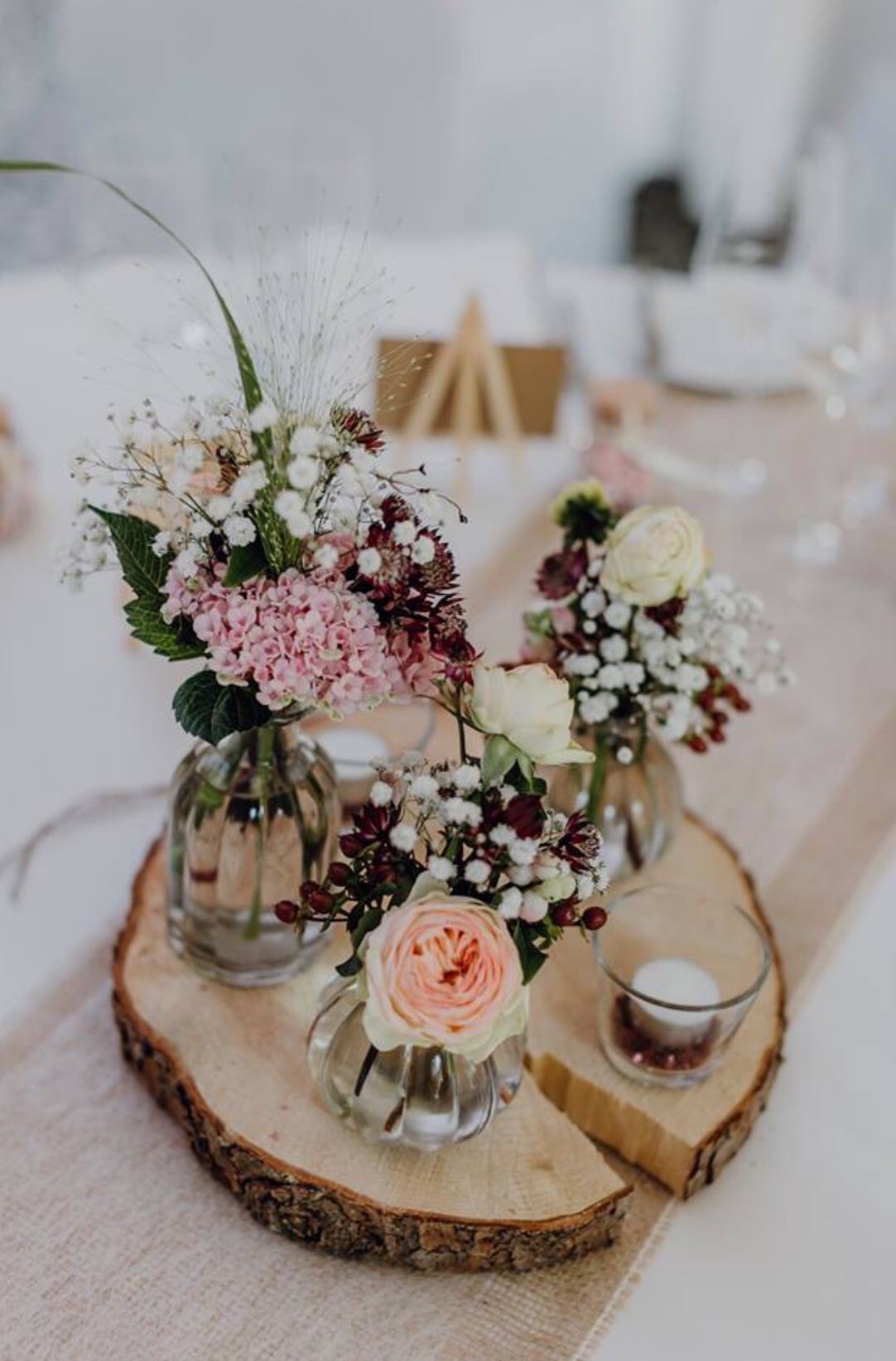 Blumenarrangement mit Rosen und Schleierkraut auf einer Holzscheibe als Symbol für die Schönheit kleiner Alltagsmomente.